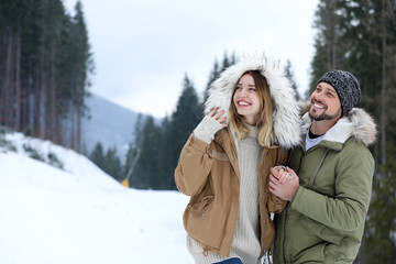 Happy couple near conifer forest on snowy day, space for text. Winter vacation