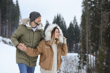 Naklejka premium Happy couple near conifer forest on snowy day, space for text. Winter vacation