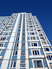 Facade of high modern blue with white residential building over cloudless blue sky bottom up vertical view