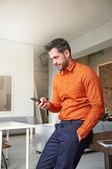 Businessman using his mobile phone and text messaging while sitting at office desk