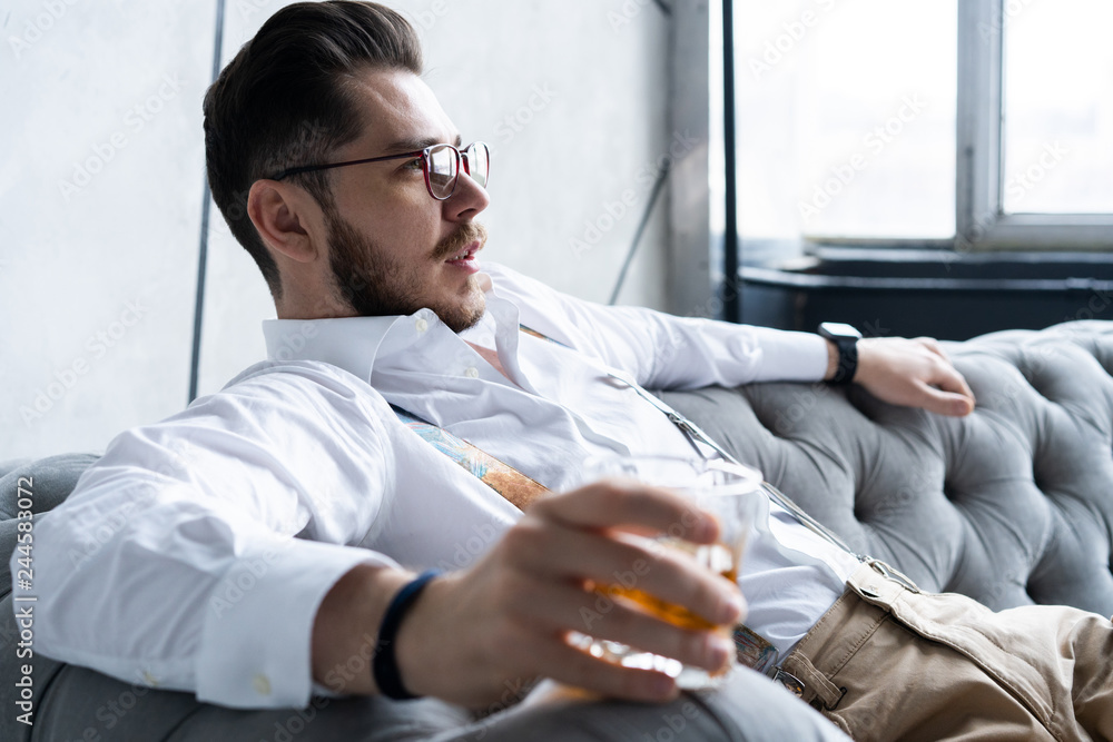 Wall mural feeling lonely. stylishly dressed young man holding a glass while sitting on sofa.