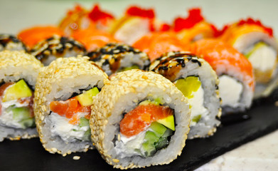Eating Sushi with chopsticks. Sushi roll japanese food in restaurant. California Sushi roll set with salmon, vegetables, flying fish roe and caviar closeup. Japan restaurant menu