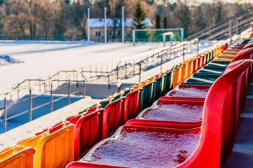 Fototapeta na wymiar Closeup of Empty Colorful Football (Soccer) Stadium Seats in the Winter Covered in Snow - Sunny Winter Day