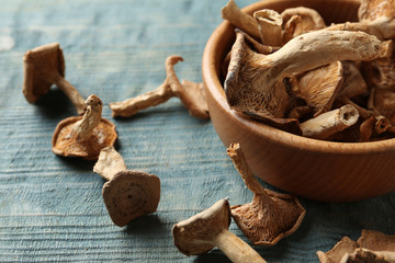 Composition of dried mushrooms and bowl on color wooden background, closeup