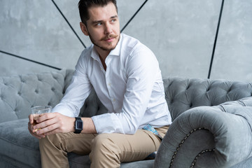 Feeling lonely. Stylishly dressed young man holding a glass while sitting on sofa.