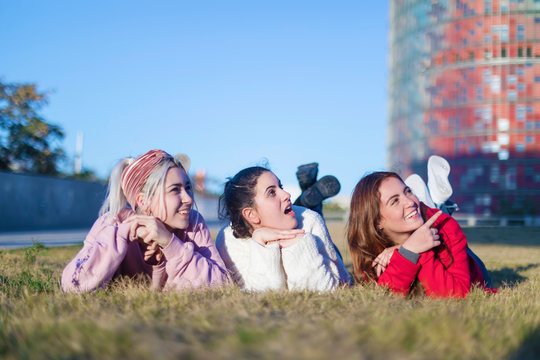 Small group of beautiful girls laughing together lying on grass outdoors in a park