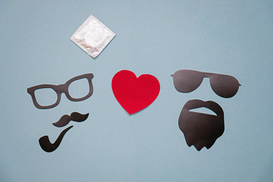 Concept photo of homosexuality: male masks with hearts and condom on blue background