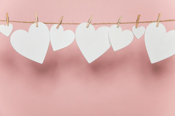 White love hearts pegged to a line against a pastel pink background