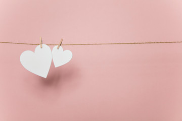 White love hearts pegged to a line against a pastel pink background