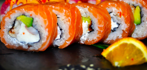 Eating Sushi with chopsticks. Sushi roll japanese food in restaurant. California Sushi roll set with salmon, vegetables, flying fish roe and caviar closeup. Japan restaurant menu