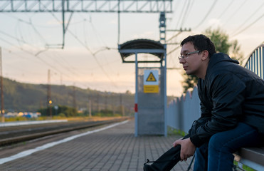 Man sitting on the street on the platform on a bench with a sad face and waiting for the train