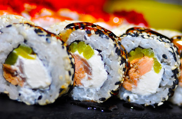 Eating Sushi with chopsticks. Sushi roll japanese food in restaurant. California Sushi roll set with salmon, vegetables, flying fish roe and caviar closeup. Japan restaurant menu