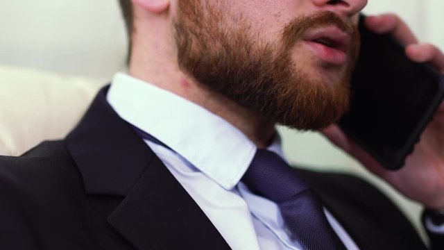Bearded businessman talking by cell phone. Only lower part of face is visible