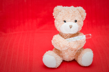 Teddy bear with a mercury thermometer on the red background