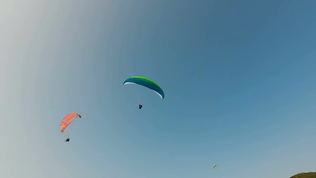 Tandem paragliders with orange and green parachutes against the blue sky