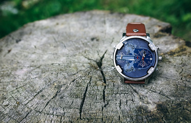Big nice elegant men's watch lying on the tree stump. Stylish fashion accessories outdoors. Copy space place.