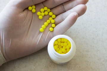 The doctor's hand in a white disposable medical glove holding a lot of yellow pills on white background