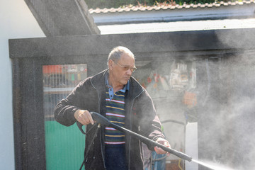 Senior man cleaning his grill ,using high pressure water.