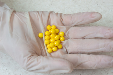 The doctor's hand in a white disposable medical glove holding a lot of yellow pills on white background