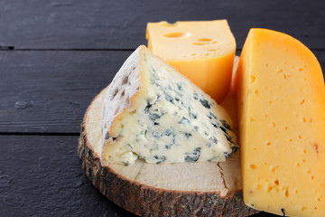 Hard cheese and blue cheese on a wooden stand. Different types of cheese on black boards. Swiss cheese and dorblu on a dark background. Copy space