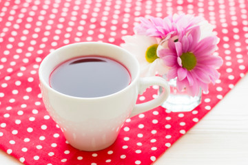 Black tea ceremony - a cup of tea, teapot, flowers on a red with white dots background