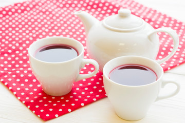 Black tea ceremony - a cup of tea, teapot, flowers on a red with white dots background