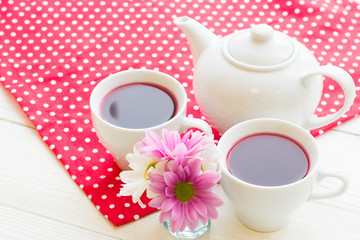 Black tea ceremony - a cup of tea, teapot, flowers on a red with white dots background