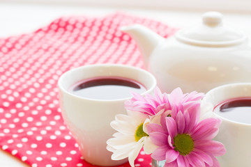 Black tea ceremony - a cup of tea, teapot, flowers on a red with white dots background