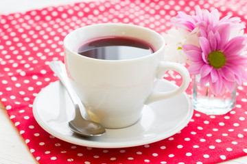 Black tea ceremony - a cup of tea, teapot, flowers on a red with white dots background