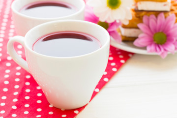Black tea ceremony - a cup of tea, teapot, sugar, cakes, flowers on a red with white dots background