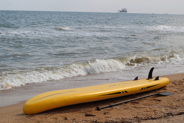 Yellow supboard lies on the sandy beach next to the paddle