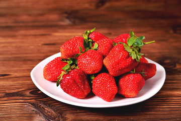 red large strawberries in a white plate on a natural brown background close-up