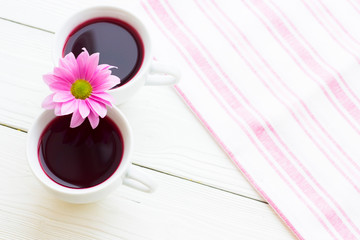 Black tea ceremony - a cup of tea, teapot, sugar, cakes, flowers on white wooden rustic background