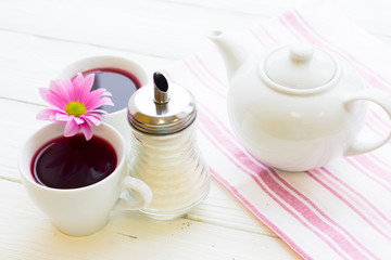 Black tea ceremony - a cup of tea, teapot, sugar, cakes, flowers on white wooden rustic background