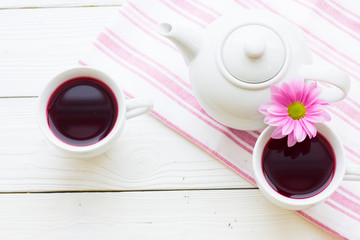 Black tea ceremony - a cup of tea, teapot, sugar, cakes, flowers on white wooden rustic background