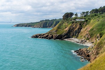 Fototapeta premium Stunning green coast on a summer day as seen from Howth Cliff Walk a popular hiking trail in Dublin, Ireland. Beautiful rugged Irish coastline under a soft light.