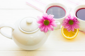 Black tea ceremony - a cup of tea, teapot, sugar, cakes, flowers on white wooden rustic background