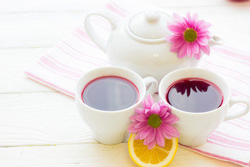 Black tea ceremony - a cup of tea, teapot, sugar, cakes, flowers on white wooden rustic background