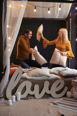 The guy and the girl are fighting with pillows on the bed.