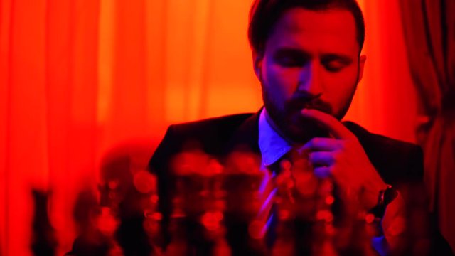 Thoughtful businessman in a business suit sitting on a blurred background pondering over strategy playing chess. Shooting in bright red light.