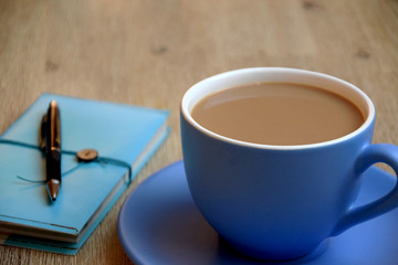 Coffee with milk in a big cup and notebook on wooden table