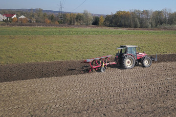 Obraz premium A farmer on a red tractor with a seeder sows grain in plowed land in a private field in the village area. Mechanization of spring field work. Farmer's everyday life. Processing of land. The agrarian.