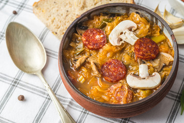 Slovak Christmas national cabbage soup in small black pot with sausage on the tablecloth background.