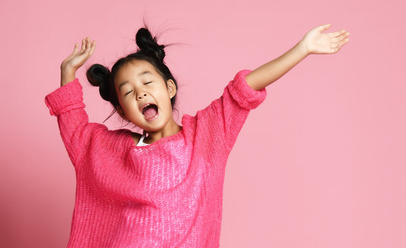 Asian kid girl in pink sweater, white pants and funny buns sings singing dancing on pink