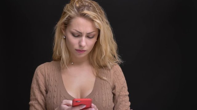 Portrait of gorgeous caucasian long-haired woman watching into smartphone with perplexity on black background.