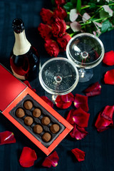 two glasses of champagne, red roses, petals and chocolates on a black background