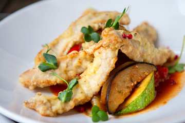 white fish fried in slices with vegetables on a white plate