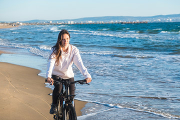 Obraz na płótnie Canvas Beautiful young woman rides a Bicycle along the sea on a sandy beach.