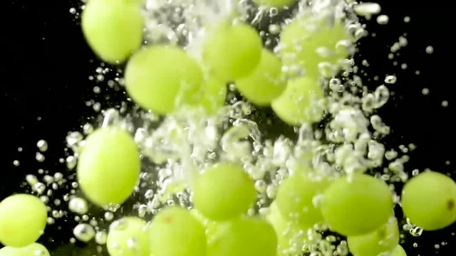 Fresh green grape falling in water with splash and air bubbles. Close up slow motion footage.