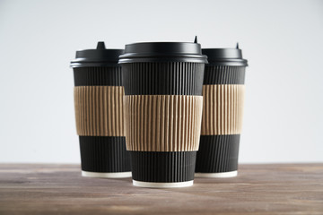 Three Paper disposable coffee black cup for take away or to go, at wooden table, space for design layout.